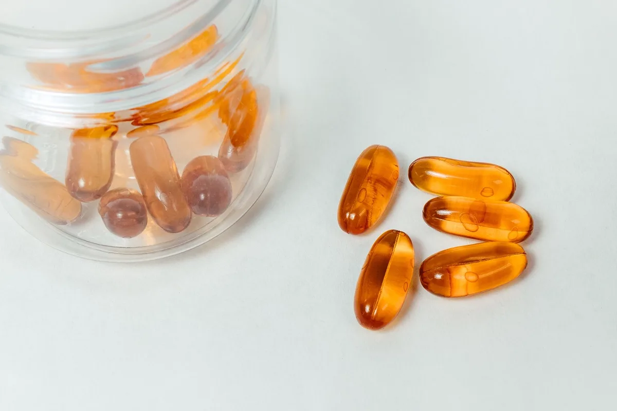 Amber capsules spilling from a clear glass container onto a pale surface