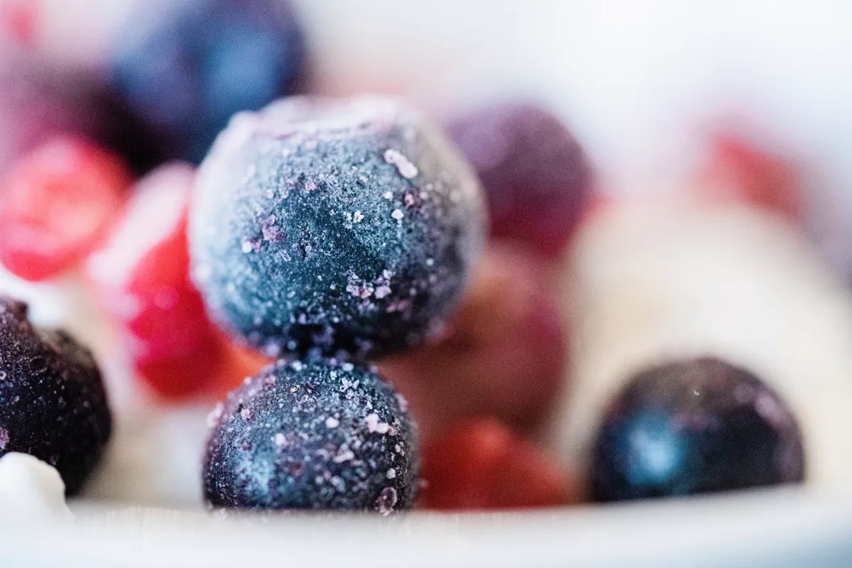 Close-up of frost-covered frozen blueberries and strawberries in a white bowl