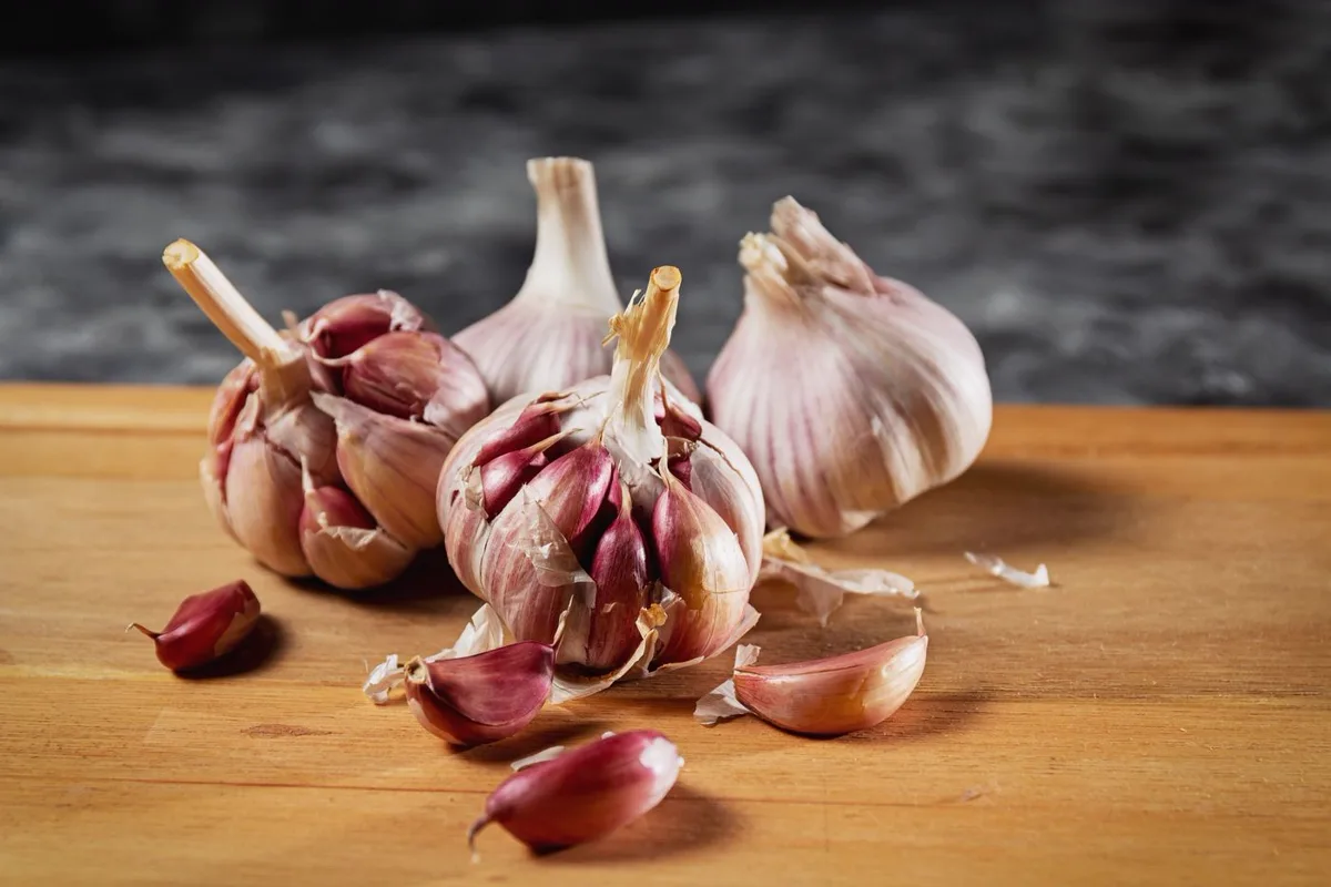 Purple-skinned garlic bulbs and loose cloves on a wooden cutting board